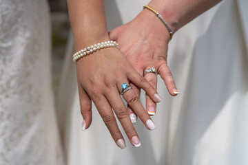 The left hands of two brides showing off their engagement and wedding rings on their wedding day. They also did their nails and wear other jewelry to accent the rings.