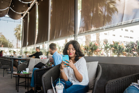 Chica chapando con su celular sentada mientas se toma una bebida fría.