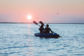 A couple of young people go in for sports in a kayak on a river or lake at sunset