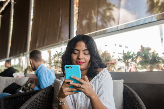 Chica chapando con su celular sentada mientas se toma una bebida fr&iacute;a.