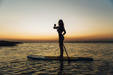 Young beautiful girl in a bikini is resting on a surfboard at sunset