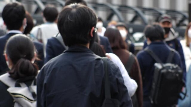 OSAKA, JAPAN - APRIL 2021 : Crowd of unidentified people wearing surgical masks to protect from Coronavirus (COVID-19) at busy downtown street. Slow motion shot. Focus in front.
