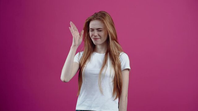 The red-haired young woman frowns and puts her hand to her nose, she smells bad. The freckled teenager, in a white T-shirt, isolated on a pink background. The concept of people's lifestyle