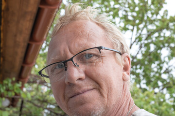 An adult mature man of European appearance with blond hair, wearing glasses, looks at the camera...