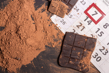 calendar close-up with broken chocolate bar and cocoa powder. World chocolate day 7 july
