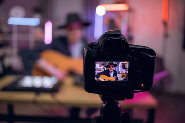 Blur background of male artist in hat and sunglasses playing guitar and recording broadcast. Focus...