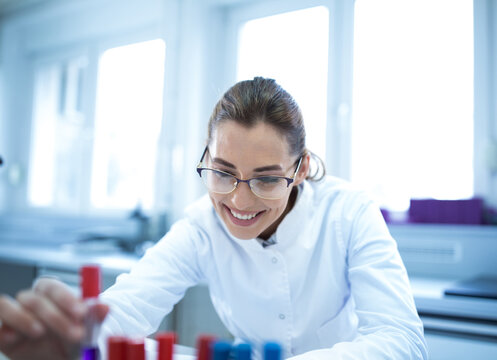 Young female scientist working in lab smiling while holding vial