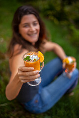 Focus on a glass of mango juice held by a woman who invites you to try it.