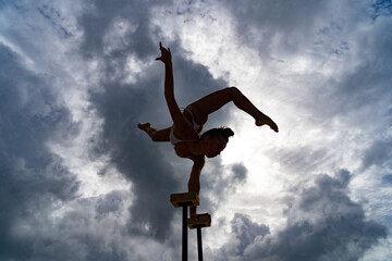 Flexible female circus Artist keep balance on hands against amazing cloudscape. Individuality, outstanding and originality.
