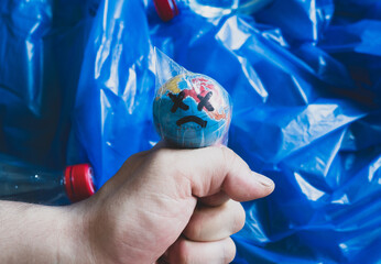 Close-up of a hand choking the globe in a plastic bag, against a background of plastic waste ....