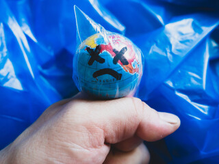 Close-up of a hand choking the globe in a plastic bag, against a background of plastic waste ....