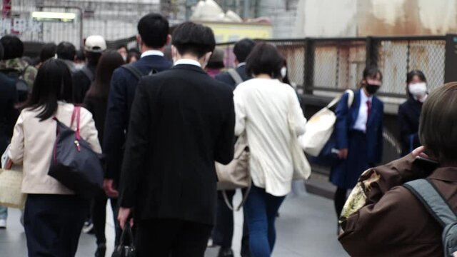OSAKA, JAPAN - APRIL 2021 : Back shot and unidentified crowd of people wearing surgical masks to protect from Coronavirus (COVID-19) at the street. Slow motion shot. In front focus.