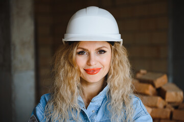 Attractive female construction worker in hardhat. Confident young specialist in checkered blue shirt in jeans standing in empty room. Interior design and renovation service.