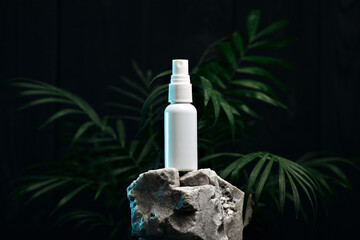 White plastic bottle spray on a white stone on a background of plants. Spray advertising photo. Mockup bottle. Black background..