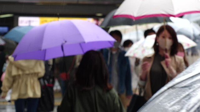 OSAKA, JAPAN - APRIL 2021 : Unidentified crowd of people wearing surgical masks to protect from Coronavirus (COVID-19) at the street. Slow motion shot in rain. In front focus.
