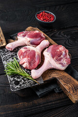 Raw Duck thighs on butcher board with meat cleaver. Black wooden background. Top view