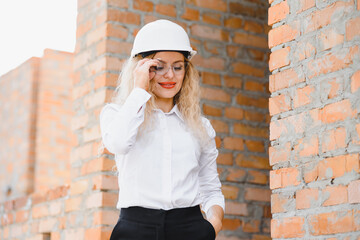 Construction engineer. Girl with construction documentation. A woman in a white hard hat against the roof of a building. Construction of a new house.