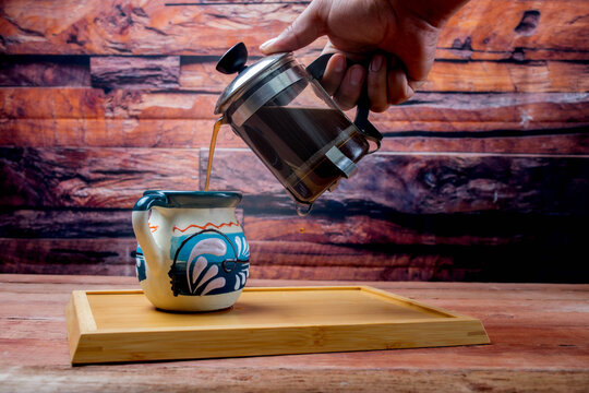 man serving coffee with french press to cup of mexican coffee on old boards