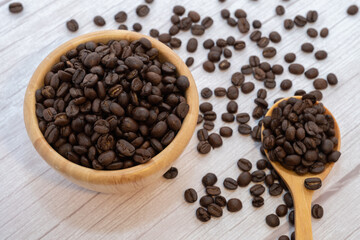 Coffee beans in wooden cup and spoon on wooden floor background.