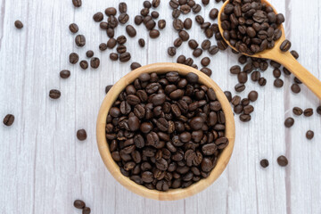 Coffee beans in wooden cup and spoon on wooden floor background.