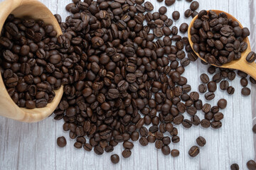 Coffee beans in wooden cup and spoon on wooden floor background.