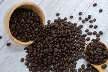 Coffee beans in wooden cup and spoon on wooden floor background.