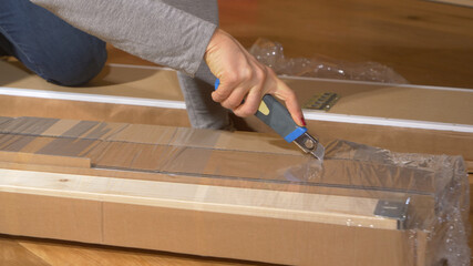 CLOSE UP: Woman cuts and peels away plastic foil off a piece of furniture.