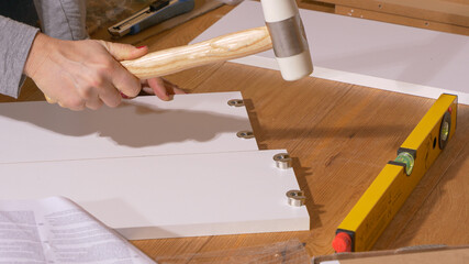 CLOSE UP: Woman hammers small metal pieces while assembling a wooden wardrobe.