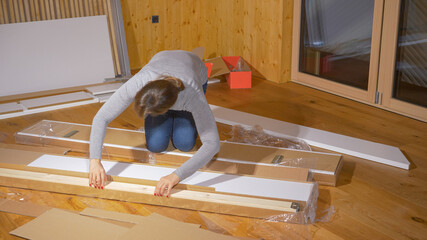 CLOSE UP: Young woman unboxes the bed frame while furnishing her new bedroom.