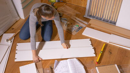 CLOSE UP: Young female moving into her new apartment assembles a white dresser.
