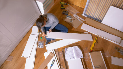 TOP DOWN Woman glues and hammers pegs into plywood board while assembling closet