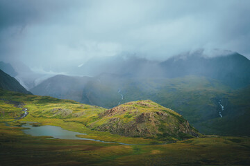 Dramatic alpine landscape with beautiful mountain lake in green valley among great rocks and high...