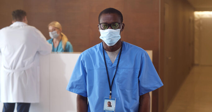 Afro-american Male Nurse Putting On Safety Mask Looking At Camera Standing In Hospital Waiting Room