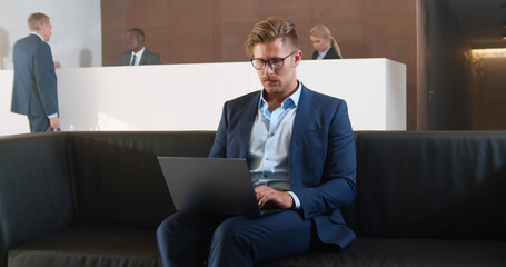 Young businessman sitting in office lobby working on laptop.