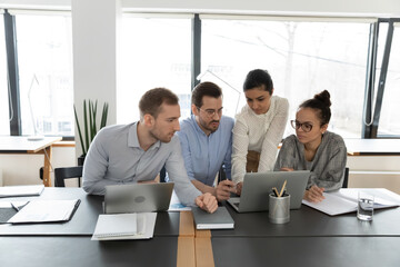 Diverse employees team looking at laptop screen, brainstorming project strategy, involved in...