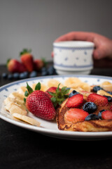 Some pancakes with sweet strawberry, blueberry and banana sliced on black table with some fruit on it 
