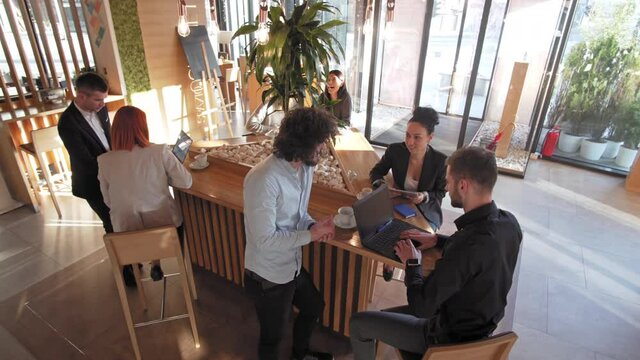 Multiracial happy friends and coworkers talking and drinking coffee at a coffee shop, enjoying pleasant conversation during a work break