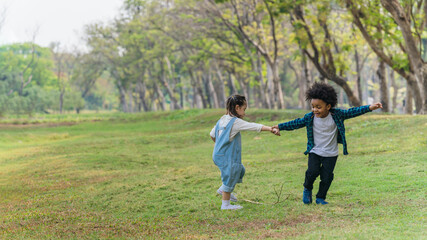 two diverse mixed race children playing and running together in park