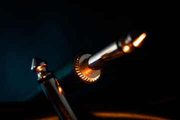 Macro Closeup of Metal Teeth at Base of Quarter Inch Jack Connector Next to Opposite End of Cord on Teal Backdrop with Orange Lighting