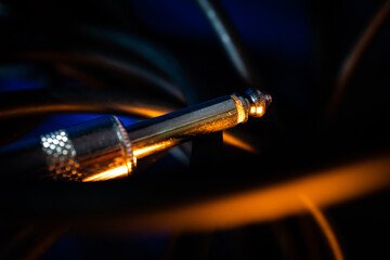 Macro Closeup of Tip on Quarter Inch Instrument Cable Connector Tangled in Cord on Blue Background with Orange Lighting