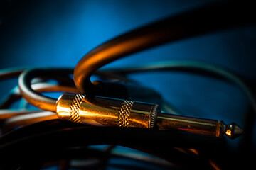 Macro Closeup of Metal Quarter Inch Instrument Cable Connector Laying Horizontally on Cord in Front of Teal Background with Orange Lighting