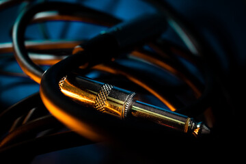 Closeup of Metal Quarter Inch Instrument Cable Connector Laying in Tangled Cord on Teal Background with Orange Lighting