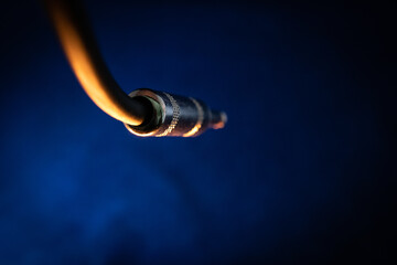 Macro Closeup of Back of Hanging Male Quarter Inch Instrument Cable Connector and Cord on Blue Backdrop with Orange Lighting