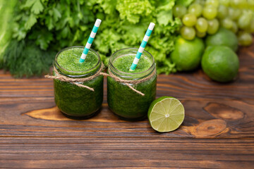 Green vegetable juice on rustic wooden table. Glasses with green organic smoothie and straw. Healthy green smoothie with spinach in a jar. Detox diet concept. Freshly blended green fruit smoothie