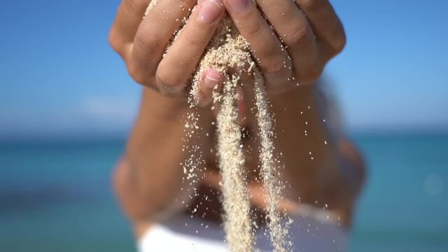 Sand falls through woman's palms on the beach with sea on background. Vacation and travel concept 