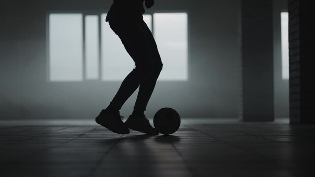 The silhouette of a football player training in an underground parking lot in the sun and rising dust. The concept of the success of sporting aspirations and perseverance. Freestyle Football