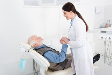 Obraz premium smiling dentist holding hands of senior patient lying in dental chair.