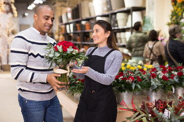 Friendly seller offering gift flower arrangement with roses to male buyer