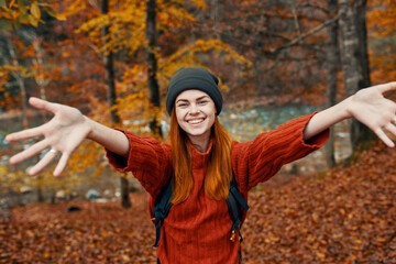 happy woman with a backpack travels in the park in autumn and gesticulate with the hands of the...