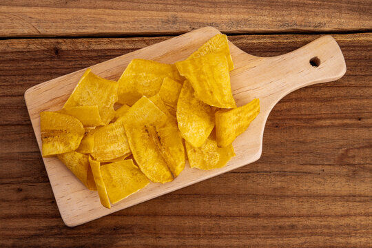 Crispy Banana Chips. Fried or baked sliced banana. Top view of typical traditional dish of Latin American gastronomy called Chifles or fried tostones on a wooden table. Roasted banana. Snack.